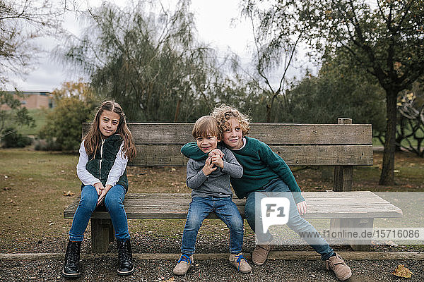 Gruppenbild von drei Kindern  die auf einer Holzbank im Freien sitzen
