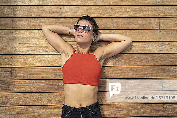 Porträt einer Frau mit Sonnenbrille  die auf dem Holzboden einer Terrasse liegt und sich entspannt