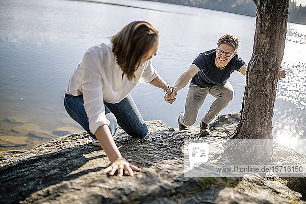 Glückliches Paar klettert Hand in Hand am Seeufer  Forstsee  Kärnten  Österreich