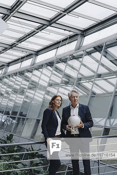 Geschäftsmann und Geschäftsfrau halten Globus in modernem Bürogebäude