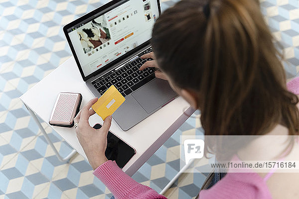 Back view of young woman using laptop and holding credit card
