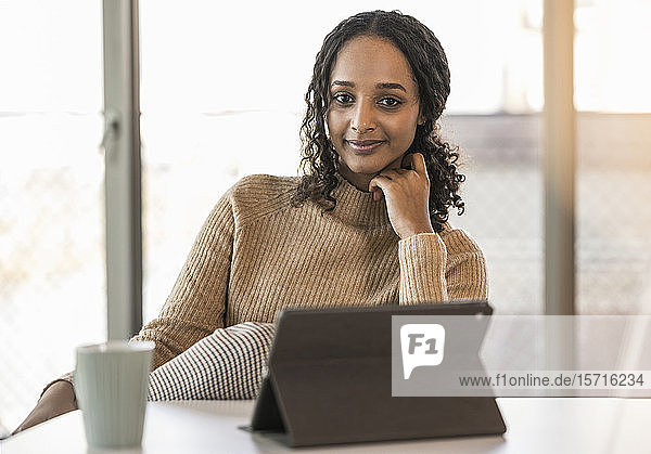 Porträt einer lächelnden jungen Geschäftsfrau  die mit einem Tablett am Schreibtisch im Büro sitzt