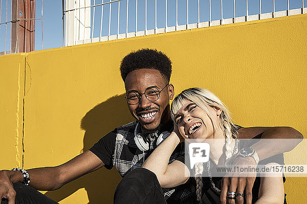 Porträt eines lachenden jungen Paares an gelber Wand