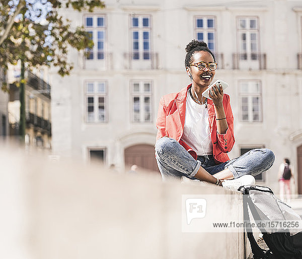 Smiling young woman with earphones and smartphone in the city  Lisbon  Portugal