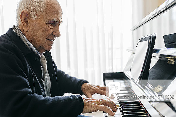 Senior man sitting in wheelchair playing piano at home