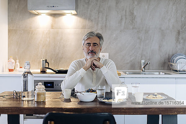 Portrait of mature man sitting at table in kitchen at home