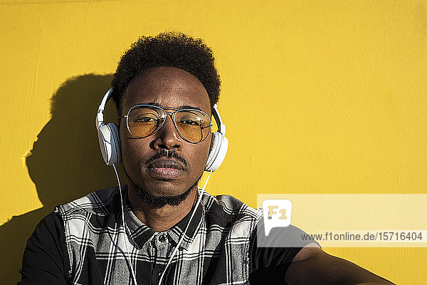 Porträt eines jungen Mannes  der mit Kopfhörern an der gelben Wand Musik hört