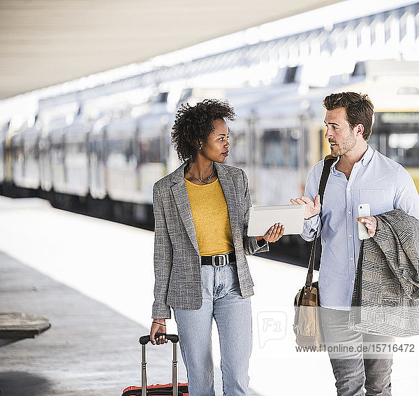 Junger Geschäftsmann und Geschäftsfrau benutzen gemeinsam Tabletten am Bahnhof