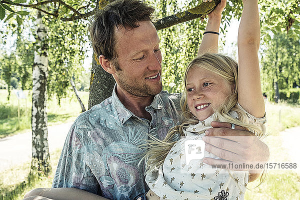 Lächelnder Vater hält Tochter an einem Birkenzweig hängend