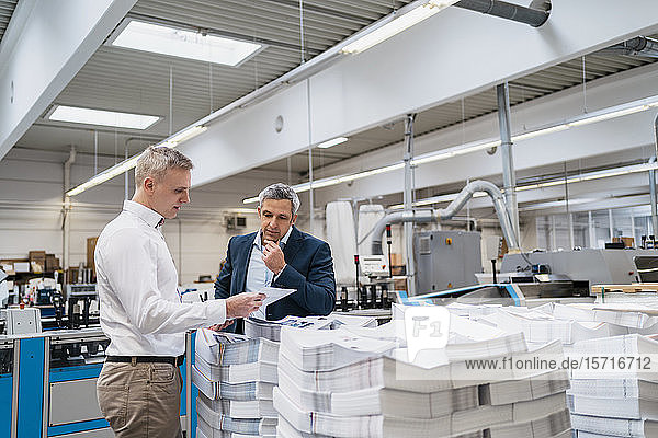 Two businessmen discussing paper in a factory