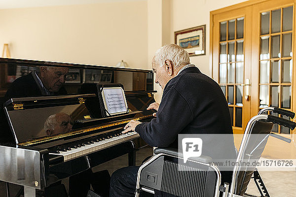 Älterer Mann sitzt im Rollstuhl und spielt zu Hause Klavier