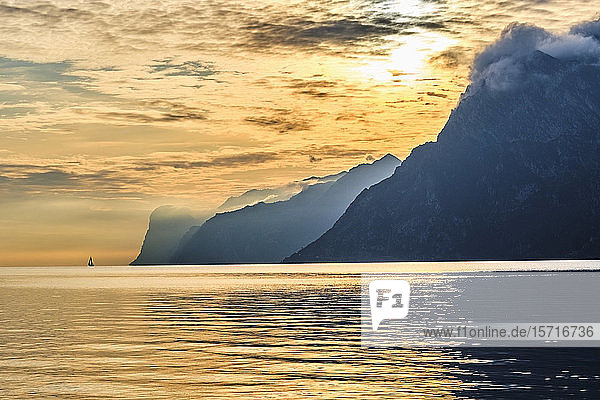 Italien  Trentino  Nago-Torbole  Silhouette eines Segelboots  das in der Nähe der Küstenklippen des Gardasees bei stimmungsvollem Sonnenaufgang segelt