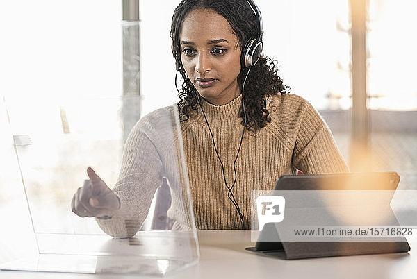 Junge Geschäftsfrau sitzt am Schreibtisch im Büro und benutzt einen transparenten Bildschirm