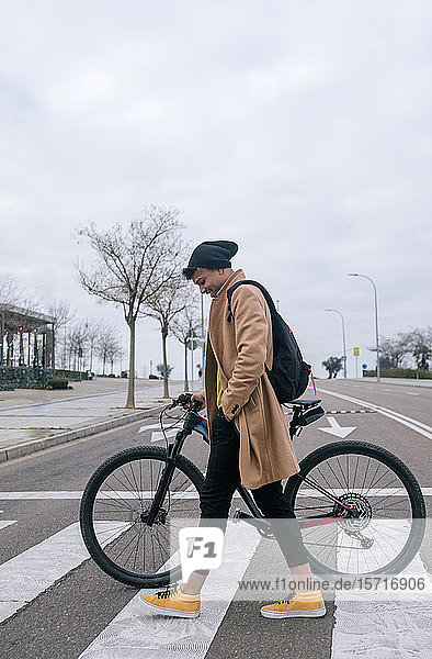 Junger Mann mit Fahrrad überquert eine Straße in der Stadt