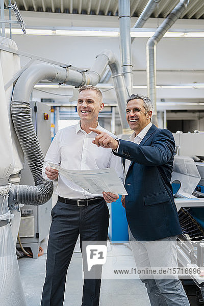 Zwei glückliche Geschäftsleute mit Papier im Gespräch in einer Fabrik