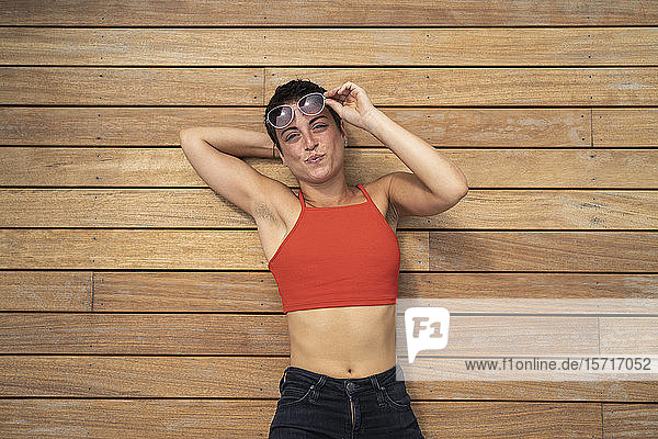 Bildnis einer Frau mit Sonnenbrille auf dem Holzboden einer Terrasse liegend