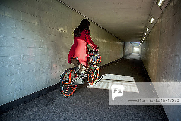 Young woman riding through an underpass on a rental bike