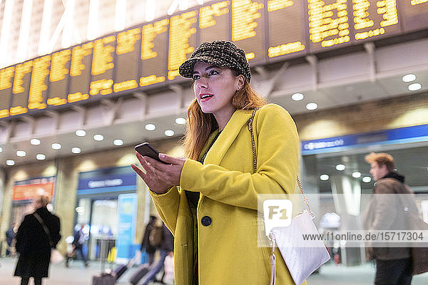Frau am Bahnhof überprüft ihr Smartphone