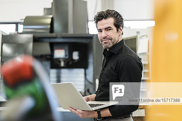 Porträt eines lächelnden Geschäftsmannes mit Laptop in einer Fabrik