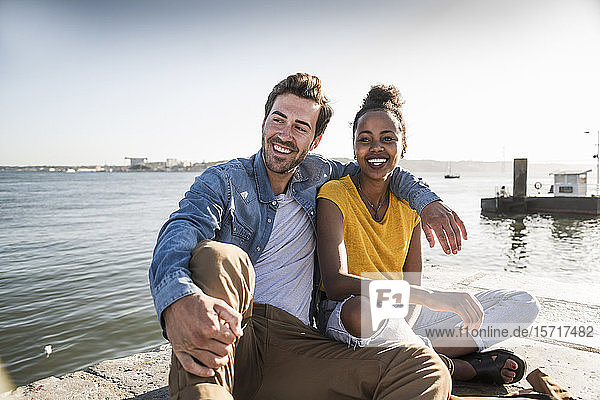 Glückliches junges Paar sitzt am Pier am Wasser  Lissabon  Portugal