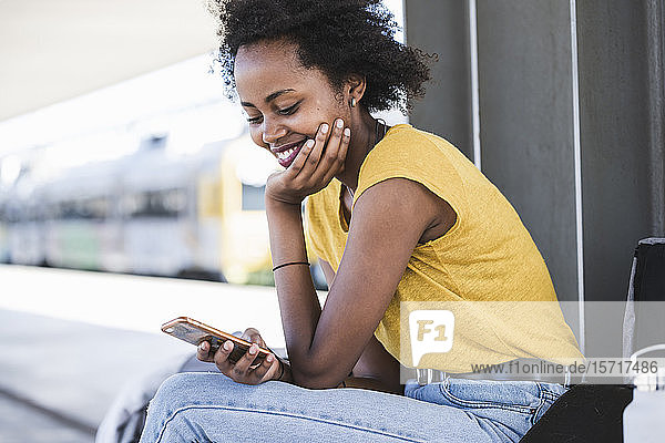 Lächelnde junge Frau benutzt Mobiltelefon am Bahnhof