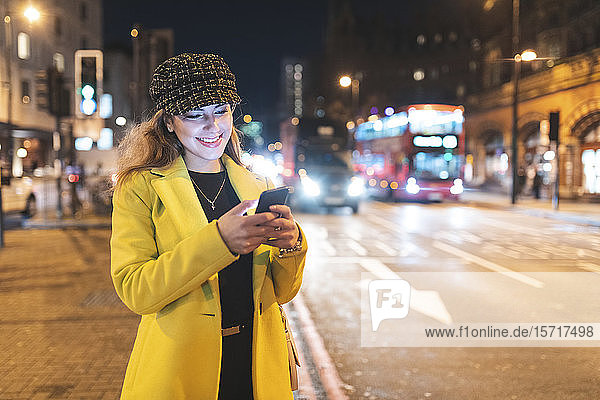 Woman with her smartphone in the city at night next to a road