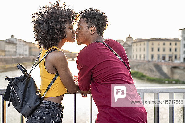 Junges Touristenpaar küsst sich bei Sonnenuntergang auf einer Brücke über dem Arno  Florenz  Italien