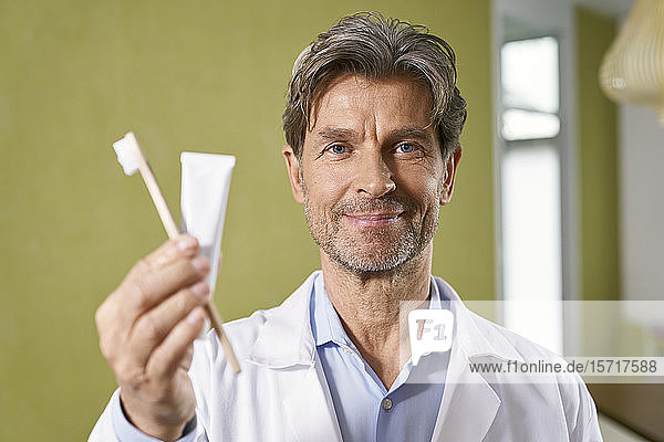 Porträt eines Zahnarztes mit Zahnbürste und Zahnpasta in seiner Praxis