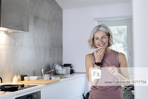 Reife Frau benutzt Mobiltelefon in der Küche zu Hause