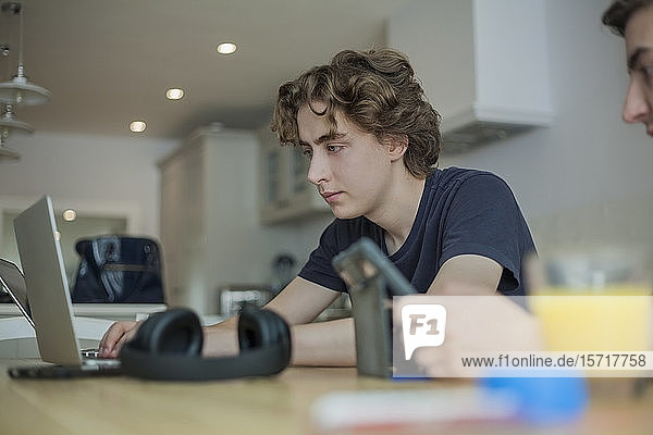 Zwei Jungen im Teenager-Alter benutzen zu Hause Smartphone und Laptop auf dem Tisch