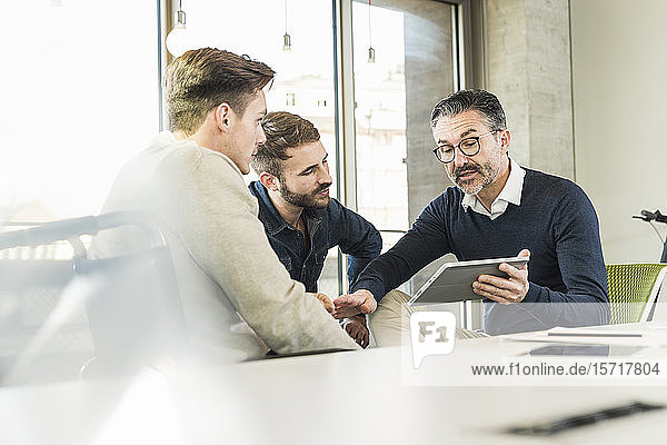 Three businessmen having a meeting in office sharing a tablet