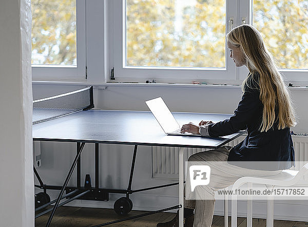 Junge Geschäftsfrau mit Laptop auf Tischtennisplatte im Büro