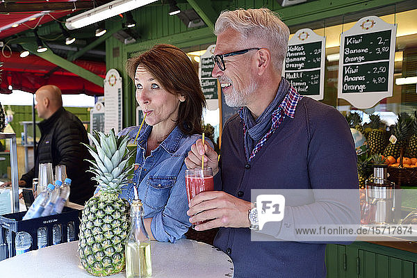Glückliches reifes Paar trinkt einen gesunden Saft an einem Marktstand