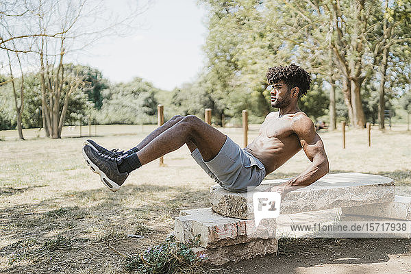 Junger Mann hebt beim Training auf Steinbank im Park die Beine