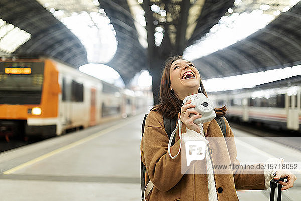 Glückliche junge Frau mit Kamera am Bahnhof