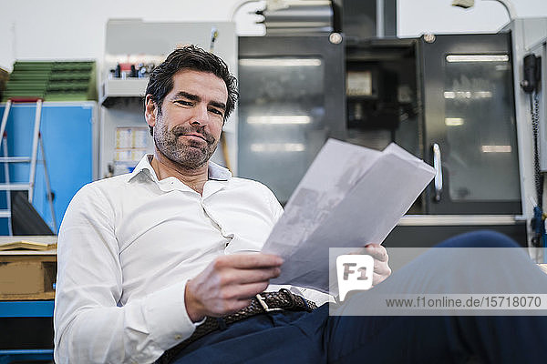 Porträt eines selbstbewussten Geschäftsmannes mit Papieren in einer Fabrik