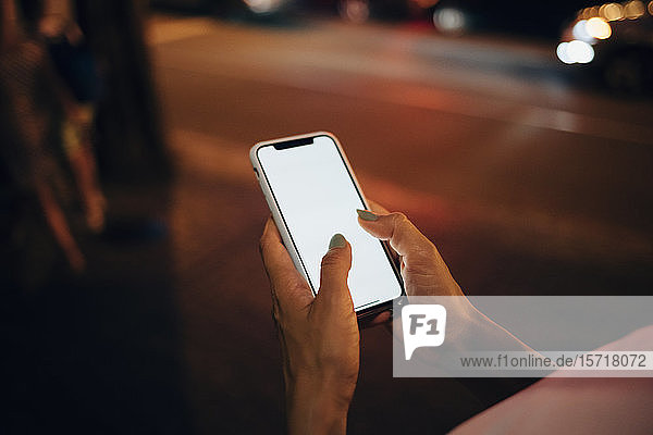 Hands of woman holding smartphone at night  close-up