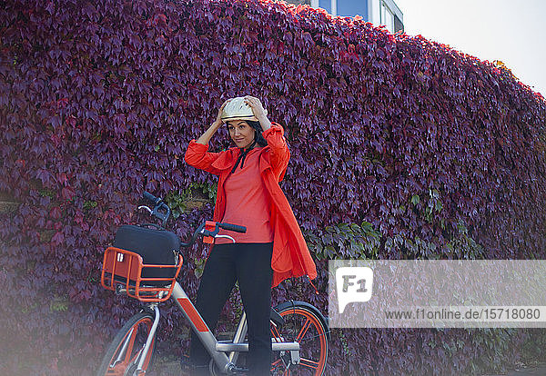 Junge Frau sitzt auf Fahrrad  setzt Schutzhelm auf