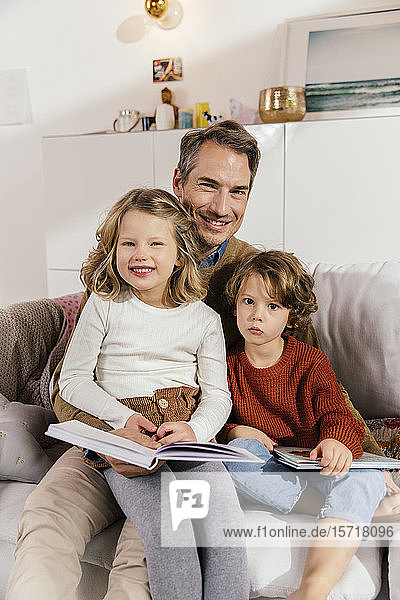 Portrait of happy father reading book with daughters on couch