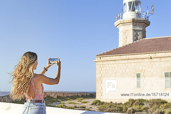 Junge Frau fotografiert den Leuchtturm von Punta Nati  Menorca  Spanien