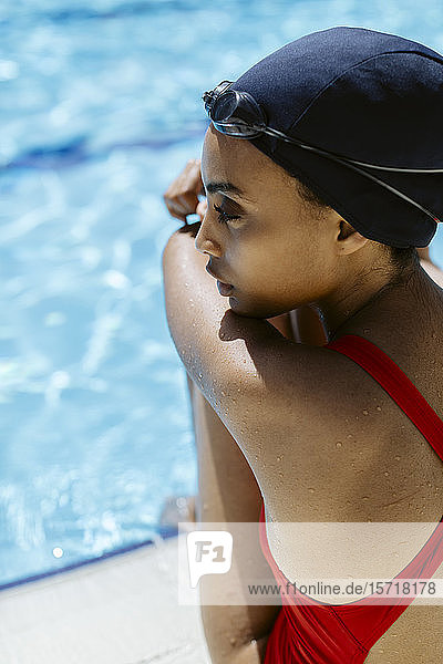 Junge Frau mit Badekappe und Schwimmbrille entspannt sich nach dem Schwimmen am Pool