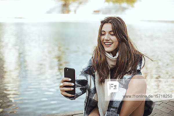Young brunette woman using smartphone and taking a selfie at lake