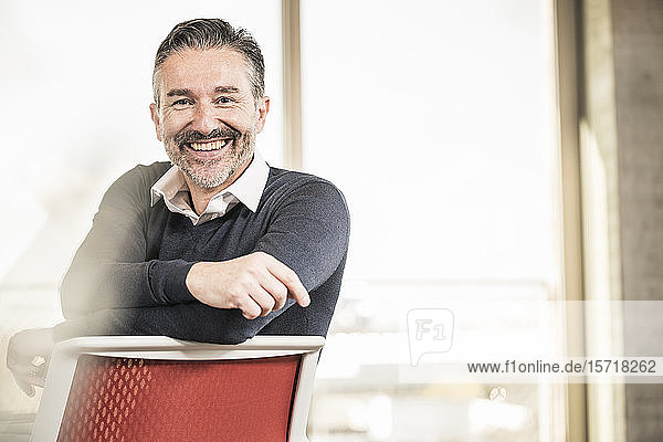 Porträt eines glücklichen reifen Geschäftsmannes  der auf einem Stuhl im Büro sitzt