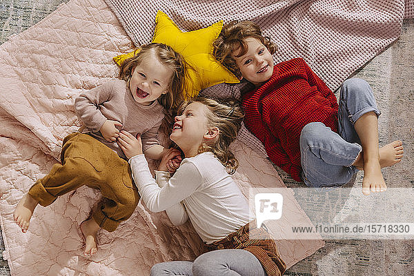 Drei glückliche Mädchen liegen zu Hause auf Decken