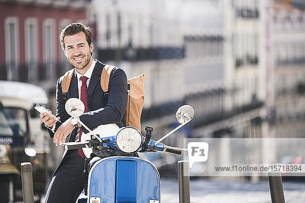 Lächelnder junger Geschäftsmann mit Handy und Motorroller in der Stadt  Lissabon  Portugal