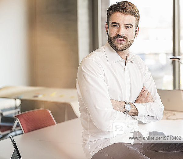Porträt eines selbstbewussten jungen Geschäftsmannes  der im Büro am Konferenztisch sitzt