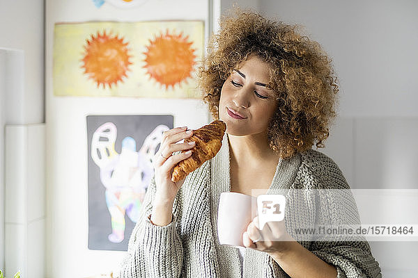 Woman eating croissant and drinking coffee at home