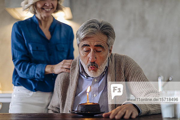 Mature couple celebrating birthday with cake in kitchen at home