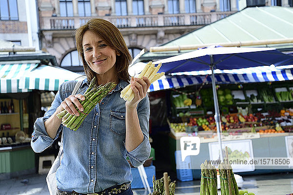 Portrait of smiling mature woman choosing asparagus at a market stall