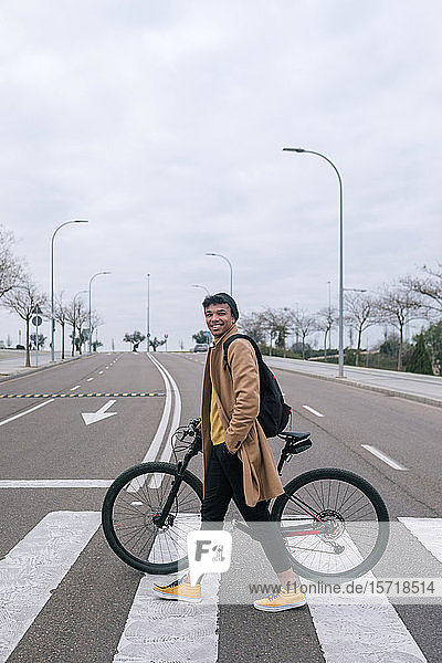 Young man with bicycle crossing a street in the city